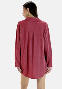 Camicia a maniche lunghe, con texture in rosso intenso; colletto abbottonato, dettaglio della piega sul retro, orlo arrotondato, realizzata in tessuto leggero.