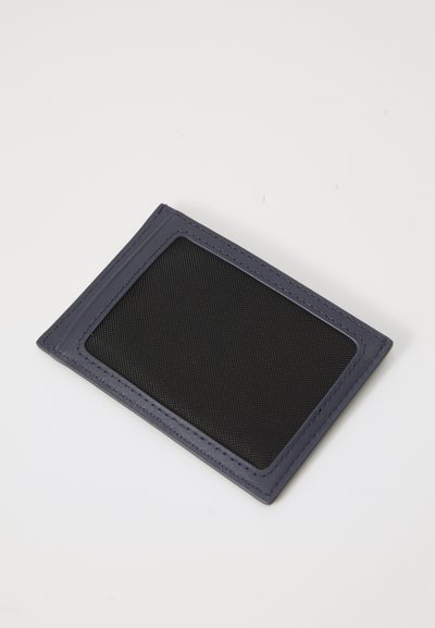 Porte-carte bleu marine avec une fenêtre en maille noire texturée et des coutures contrastées. Design rectangulaire slim, léger et fonctionnel.