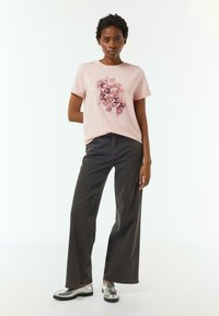 Pink cotton t-shirt with floral graphic and lettering, paired with high-waisted dark gray wide-leg jeans and silver loafers.