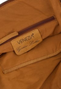 Intérieur d'un sac en cuir marron avec une poche zippée. Étiquette avec les inscriptions "VENEZIA" et "Cuir véritable". Texture lisse, détails de couture minimaux.