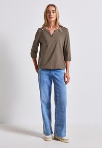 Oliivinvihreä, kolme neljännesosa-hihaista paitaa, jossa on V-pääntie. Yhdistetty vaaleansinihin leveälahkeisiin denim-farkkuihin. Sileä pinta ja rento istuvuus.