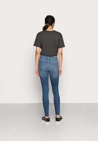 Camisa negra de manga corta, jeans ajustados azules y zapatillas Vans negras. Tela suave con un ajuste casual; bolsillos traseros grandes en los jeans.