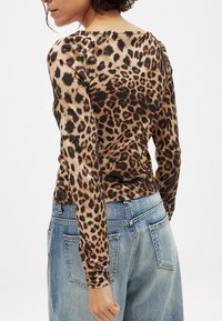 Pikkade varrukatega topp läbipaistvast, kerge materjalist, millel on beež ja pruun leopardimuster. Kombineeritud kõrge vöökohaga helesinise teksapükstega.