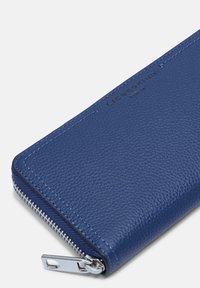 Portefeuille en cuir bleu avec une finition texturée, doté d'une fermeture éclair en métal argenté, d'un logo en relief et de lignes épurées.