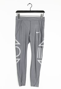 Šedé sportovní legíny z elastického materiálu. Mají bílou Nike logo a velké geometrické vzory v světle šedé na bocích.