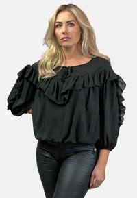 Czarna bluzka z falbaniastymi rękawami, wykonana z lekkiego materiału, okrągły dekolt i detal w postaci wiązania. Stylizowana z czarnymi dopasowanymi spodniami. Miękka w dotyku.