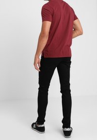 Camisa corta de manga en color marrón con un patrón texturizado, combinada con pantalones ajustados negros y zapatillas negras con detalles blancos.