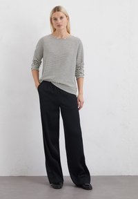 Gestreepte langlopende blouse in crème en zwart; relaxte pasvorm. Gecombineerd met losse zwarte broeken; gladde stof, wijd beenontwerp. Platte schoenen.