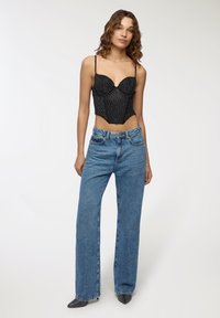 Top corsetto nero a pois con spalline sottili, abbinato a jeans a gamba larga leggeri di colore azzurro a vita alta e tacchi a punta neri.