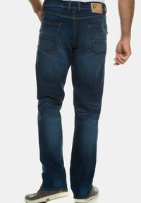 Vaqueros de mezclilla índigo con diseño de pierna recta, cinco bolsillos y costuras reforzadas. La etiqueta en la cintura trasera dice "JP."