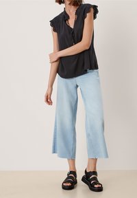 Blusa nera senza maniche con bordo in pizzo, abbinata a jeans a gamba larga blu chiaro e sandali neri con suola spessa e dettagli con fibbia.