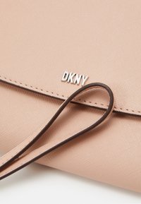 Růžová strukturovaná umělá kabelka se stříbrným logem DKNY, která má hnědý popruh a klopu.