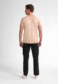 Světle béžové tričko s krátkým rukávem, černé cargo kalhoty s bočními kapsami a béžové tenisky. Materiál vypadá jemně; střih je ležérní.