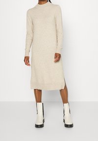 Beige, stickad klänning med slim fit, långa ärmar, ribbade manschetter och sidoflärpar. Matchad med vita och svarta ankelstövlar.