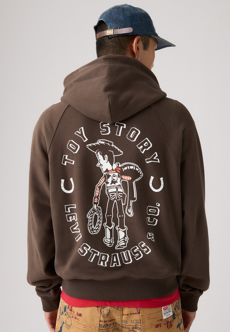 Felpa marrone con cappuccio, caratterizzata da una grafica di un cowboy con una corda, stampata in bianco, e il testo "TOY STORY LEVI STRAUSS." Tessuto morbido.