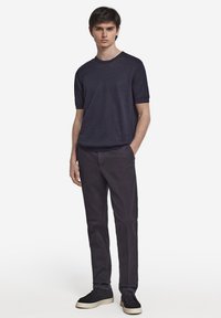 Marinblå kortärmad skjorta kombinerad med mörkgrå byxor och svarta sneakers. Enkel design med rundad halsringning och välstrukturerad passform.