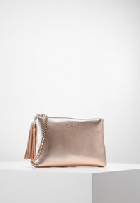 Pequeño bolso de mano metálico en color oro rosa con cadena dorada y borla, exhibido sobre un pedestal blanco contra un fondo liso.