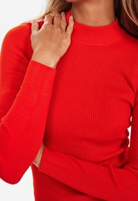 Rotes geripptes Langarmoberteil mit hohem Kragen und figurbetonter Passform. Verfügt über einen strukturierten Stoff und verlängerte Ärmel.