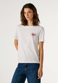 T-shirt blanc en coton avec un col rond, des manches courtes et un graphique rose imprimé sur le devant. Présente des textures subtiles et une coupe décontractée.