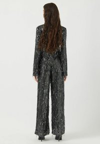 Zwarte pailletten jumpsuit met franjes, voorzien van lange mouwen en wijde pijpen, ontworpen met verticale zilveren accenten.