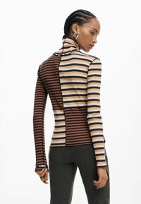 Triibuline pika varrukaga kaelusega top, värvitoonides pruun, must ja beež. Omaduseks on keha järgnev lõige, sooniline tekstuur ja kontrastsed plaastrid.