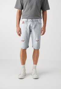 Lyseblå denimshorts med avslappet passform, med slitte detaljer og frynsete kanter. Kombinert med hvite joggesko og grå sokker.