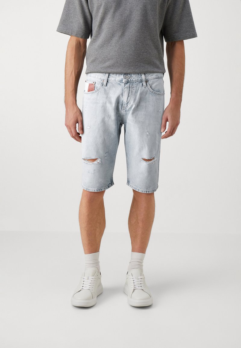 Lyseblå denimshorts med avslappet passform, med slitte detaljer og frynsete kanter. Kombinert med hvite joggesko og grå sokker.