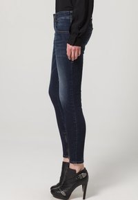Mörkblå skinny jeans i denim med hög midja, subtila blekningar och sidodetaljer med dragkedja. Kombineras med svarta ankelskor.