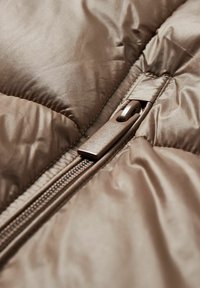 Brun pufferjakke lavet af stof med en glat, blank tekstur. Har en brun lynlås og syninger, med quiltede sektioner synlige.