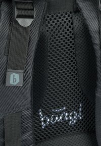 Tessuto a rete nero con finitura testurizzata, caratterizzato da un'etichetta con logo "b" e cuciture visibili. Include spalline regolabili per una personalizzazione.