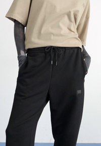 Beige katoenen T-shirt met korte mouwen, gecombineerd met zwarte joggerbroeken met een trekkoord in de taille en een klein logo-label.