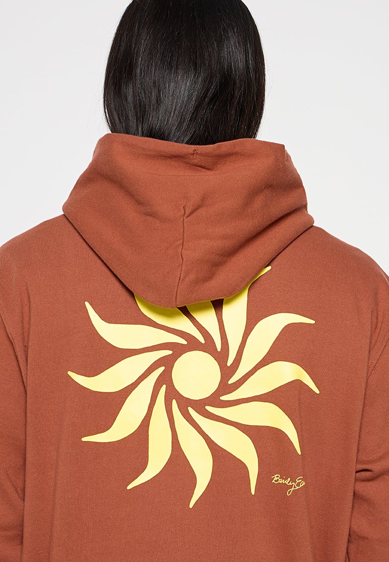 Hoodie marron avec un grand design de soleil jaune à l'arrière. Doté d'une capuche avec cordon de serrage et d'un tissu doux et texturé.