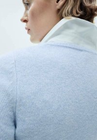 Light blue knit sweater with a soft texture, featuring a high collar and a white shirt underneath, emphasizing layered styling.