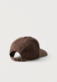 Καφέ βαμβακερό καπέλο μπέιζμπολ με κυρτή γείσο, ρυθμιζόμενο λουράκι και μεταλλική αγκράφα. Η υφή του υφάσματος φαίνεται απαλή με διακριτικές ραφές.