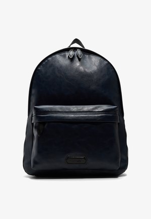 Marinblå läderryggsäck med en slät textur, rundad form, framficka med dragkedja och dubbla dragkedjor upptill. Har en diskret logotypaccent.