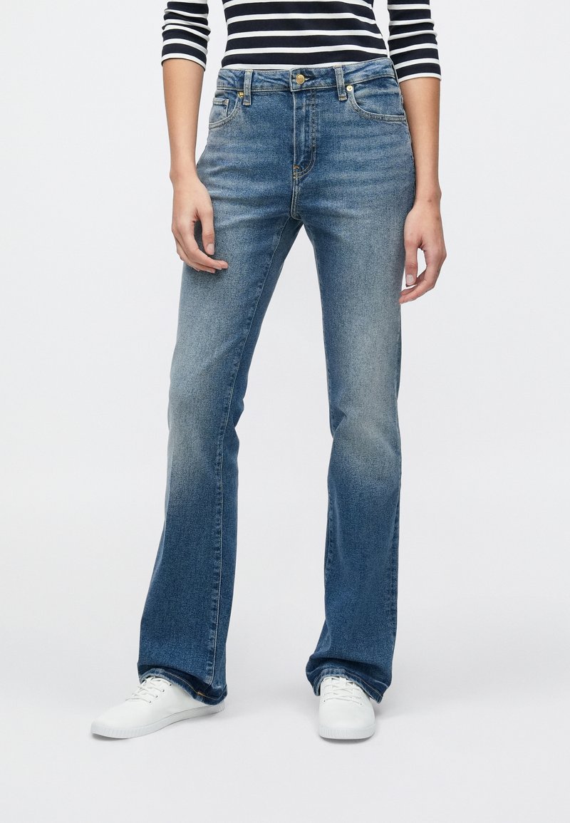 Τζιν με ξεθωριασμένο γαλάζιο χρώμα και φαρδιά γραμμή, κατασκευασμένα από τζιν ύφασμα. Διαθέτουν μέση μεσαίου ύψους, πέντε τσέπες και μεταλλικά στοιχεία σε χρυσούς τόνους. Συνδυάζονται με λευκά αθλητικά παπούτσια.