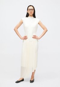 Λευκό, εφαρμοστό φόρεμα με ψηλό γιακά και πλισέ φούστα, με έκδηλο ασύμμετρο τελείωμα. Φορεμένο με μαύρες μπαλαρίνες και γυαλιά.