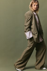 Olīvu zaļš pārsteidzīgs žakets un saskaņotas plaša griezuma bikses, stilizētas ar gaisīgu svītrains kreklu, kas piedāvā lielus manšetes un gludu auduma tekstūru.