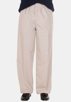 Pantaloni beige a gamba larga con pieghe, chiusura con bottone e zip, indossati con mocassini neri con nappine e un top scuro.