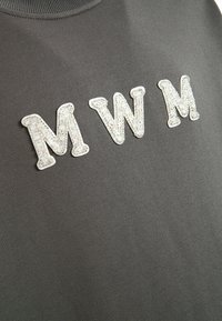 Sudadera gris con tres grandes letras "MNM" brillantes y decoradas con strass en la parte frontal, con cuello de canalé y textura suave.