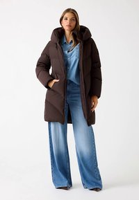 Bruine pufferjas met een hoge kraag en ritssluiting, met een doorgestikt design. Gecombineerd met wijde, lichtgewassen spijkerbroeken.