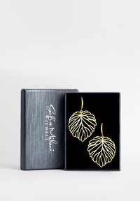 Guldbladformade örhängen visade upp i en svart sammetstoppad box, med intrikata utskärningsmönster och en slät, glänsande yta.