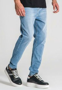 Ljust blå denimjeans med slim fit, i kombination med svarta sneakers med vita detaljer och snören, visade i stående ställning.