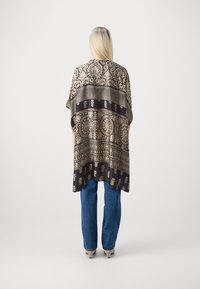 Svart og gullmønstret kimono med vide ermer, med intrikate blomsterdesign og en løs passform, kombinert med blå denimbukser.