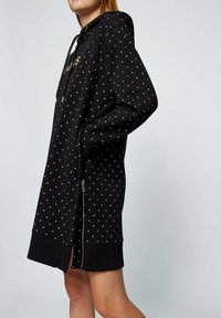 Černá mikinová šaty s zlatými puntíky, dlouhé rukávy, nastavitelná kapuce se šňůrkou, boční zip, žebrované manžety a lem.