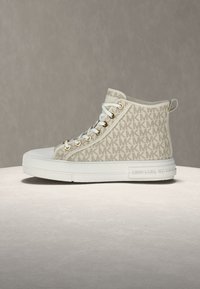 Beiger High-Top-Sneaker aus Segeltuch mit weißer Gummisohle, versehen mit einem sich wiederholenden "MK"-Logo-Muster, goldenen Ösen und Schnürverschluss vorne.