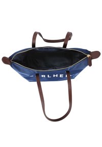 Sac fourre-tout en tissu marine avec des anses en cuir marron, une fermeture éclair dorée et un intérieur noir. Comprend un texte imprimé sur le côté et une ouverture spacieuse pour le contenu.