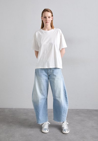 White cotton t-shirt with loose fit, paired with light blue wide-leg jeans featuring a frayed hem, and silver sneakers. Simple, casual look.