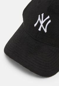 Fekete bolyhos sapka, texturált felülettel, ívelt karimával és fehér hímzett 'NY' logóval az elején.
