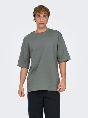 T-shirt gris oversize en tissu doux, avec manches courtes et encolure ronde. Associé à un pantalon noir à coupe ample.